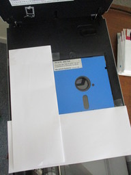 A flatbed scanner with a taped-together paper jig holding a disk at the proper offset from the corner.